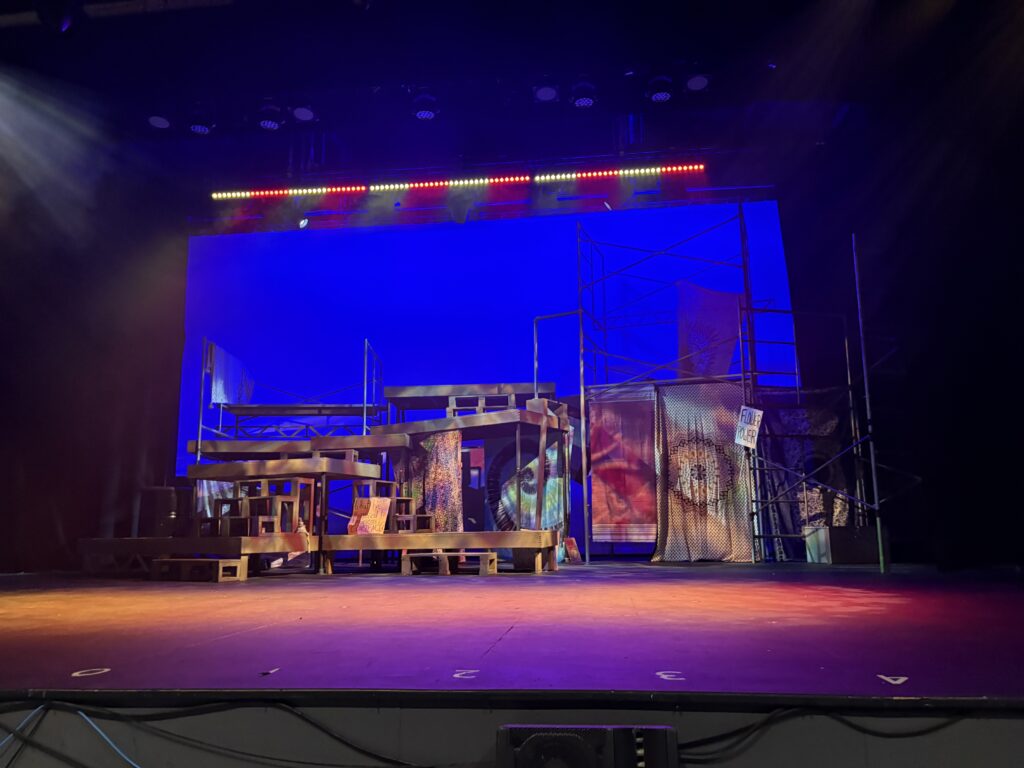 The stage of Hair. Wood pallets and metal scaffolding contrasting with the softness of blankets and picketing signs